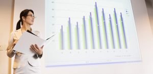 Image of business woman presenting the business case for accessible communications with statistics projected on a screen behind her.
