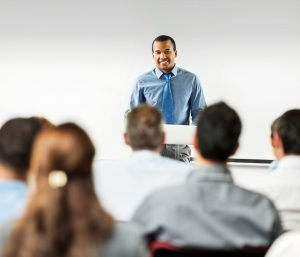 Man smiling and standing at a podium in front of an audience.