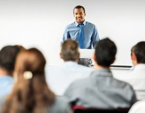 Man smiling and standing at a podium in front of an audience.