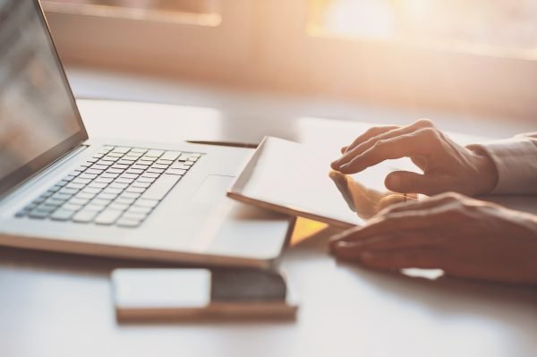 Image of hands scrolling accessible content on a mobile device with a mobile phone and laptop on a desk.