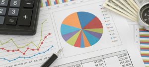 Image of standard print financial documents with a pie chart, table and graphs, a calculator, a pen, a compass and cash, showing how T-Base makes America’s top financial institutions accessible.