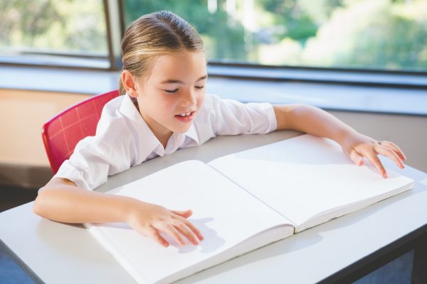 Image of a k-12 student reading a braille textbook in a classroom