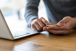 Image of hands at a desk in front of a laptop making a call on a mobile device, contacting T-Base