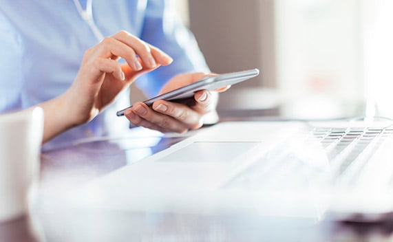 Image of hands typing on a mobile device infront of a laptop