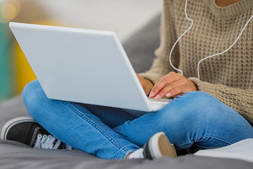 Image of a person seated on a bed, typing on their laptop