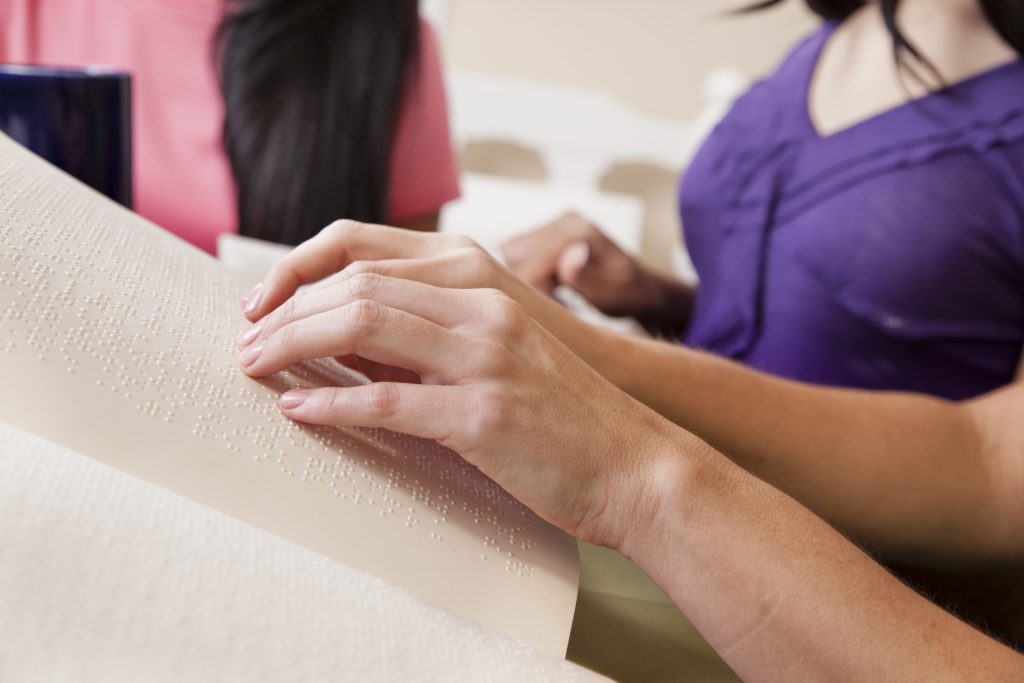 Braille printing services produced by T-Base. Image is of a person's hands reading a from a book.